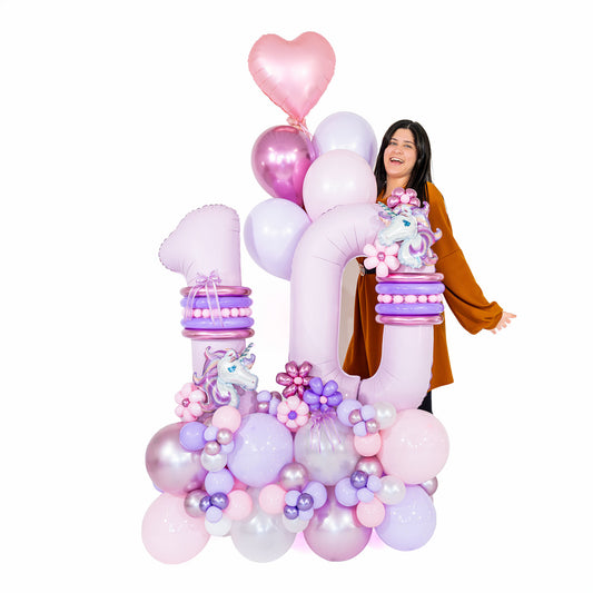 Woman standing behind a pink and lilac unicorn number 10 balloon arrangement with balloon flowers and a heart balloon.