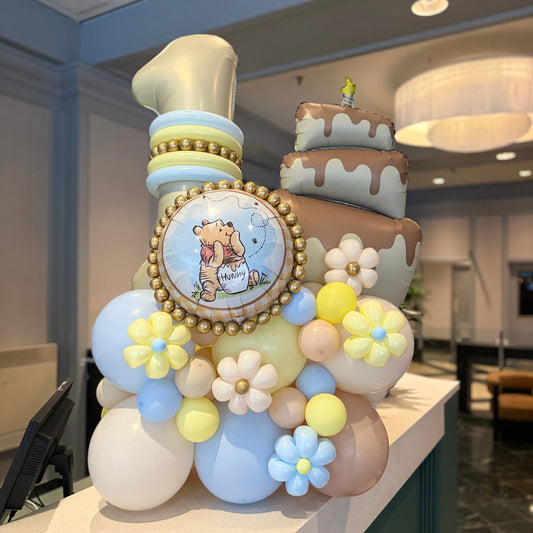 Winnie the Pooh first birthday balloon arrangement with a cream number 1, cake balloon, pastel blue and yellow balloons, flowers and gold accents in Toronto.