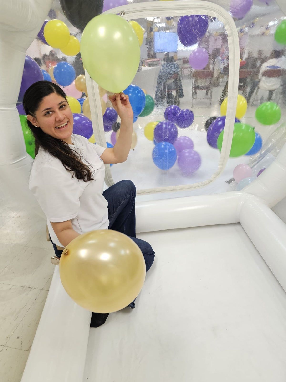 Woman holding balloons inside an inflatable bouncy castle with colorful balloons.