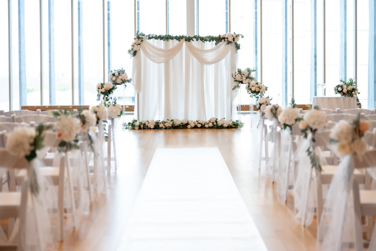 A beautifully decorated wedding ceremony space with floral arrangements, fabric drapes, and lighting installations.
