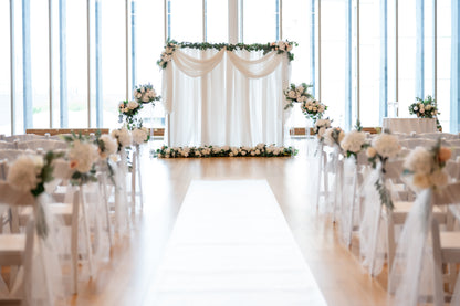 A beautifully decorated wedding ceremony space with floral arrangements, fabric drapes, and lighting installations.
