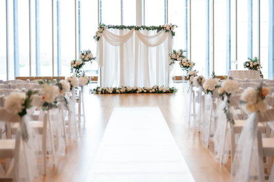 A beautifully decorated wedding ceremony space with floral arrangements, fabric drapes, and lighting installations.