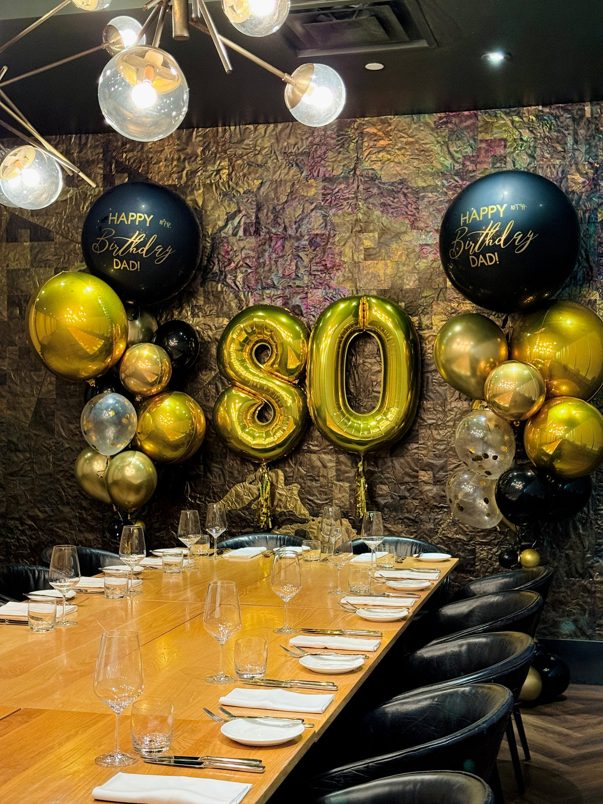 Decorated birthday table with balloons and 'Happy Birthday Dad!' text against a textured wall.