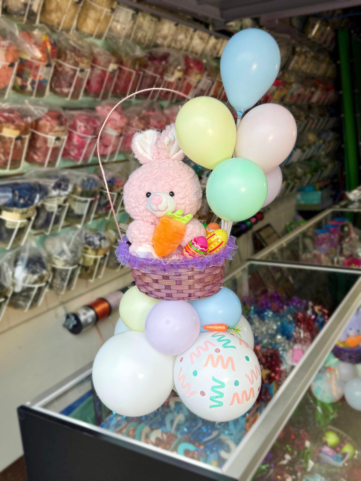 Decorative display with a plush bunny, balloons, and Easter eggs in a store setting.