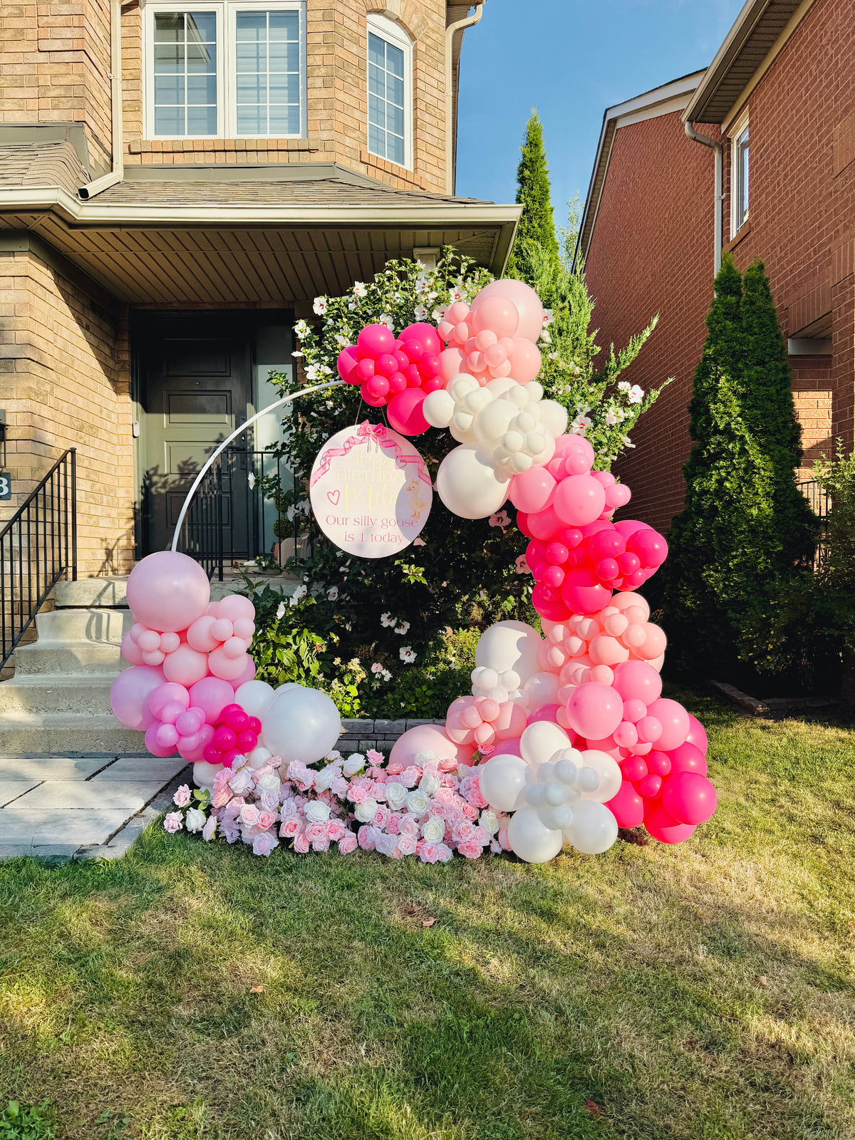 Balloon arch with pink, white, and red balloons in front of a house.