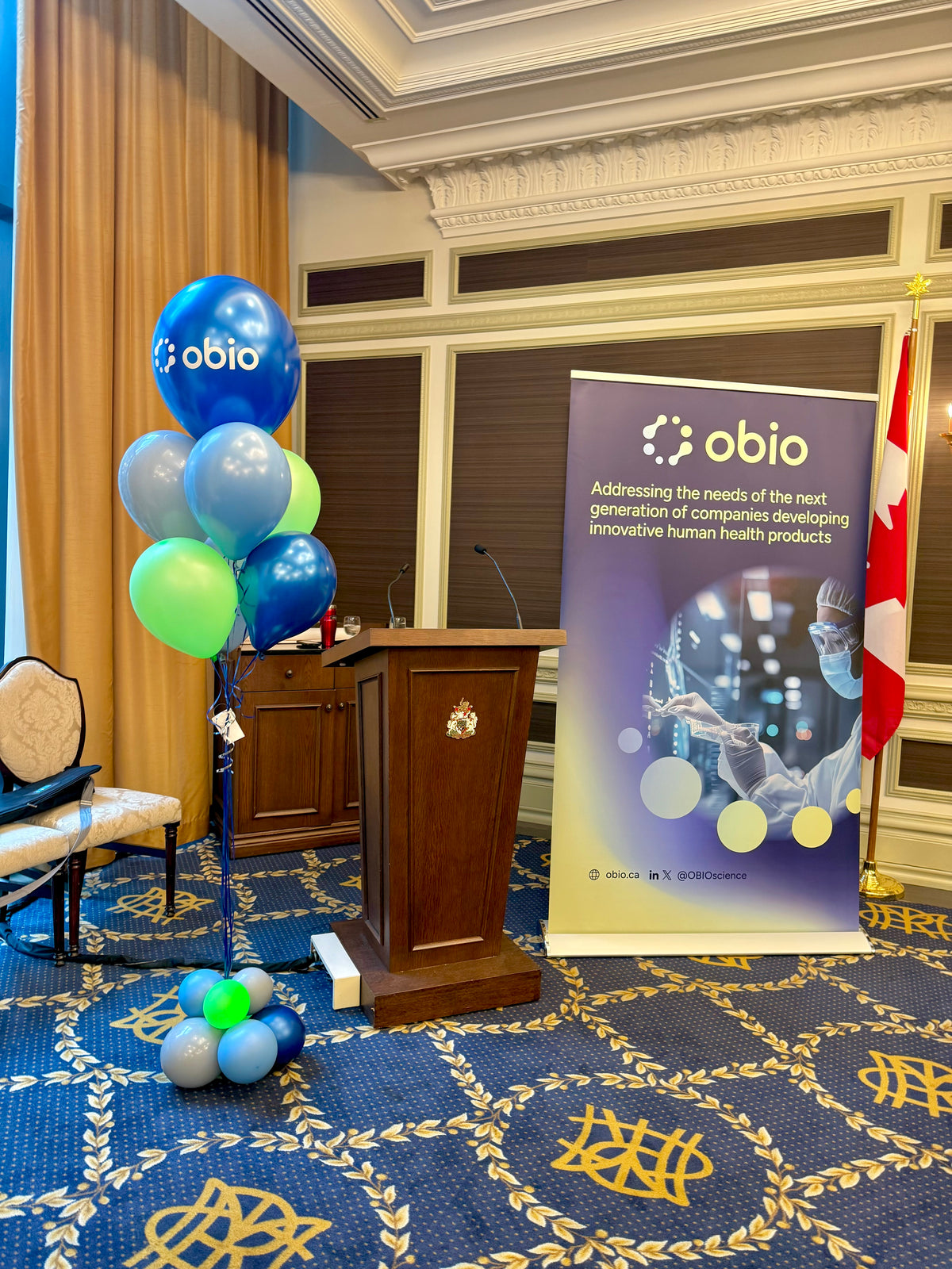 A balloon bouquet arrangement with multiple balloons including a prominent balloon with a logo, displayed in a room with a presentation setup.