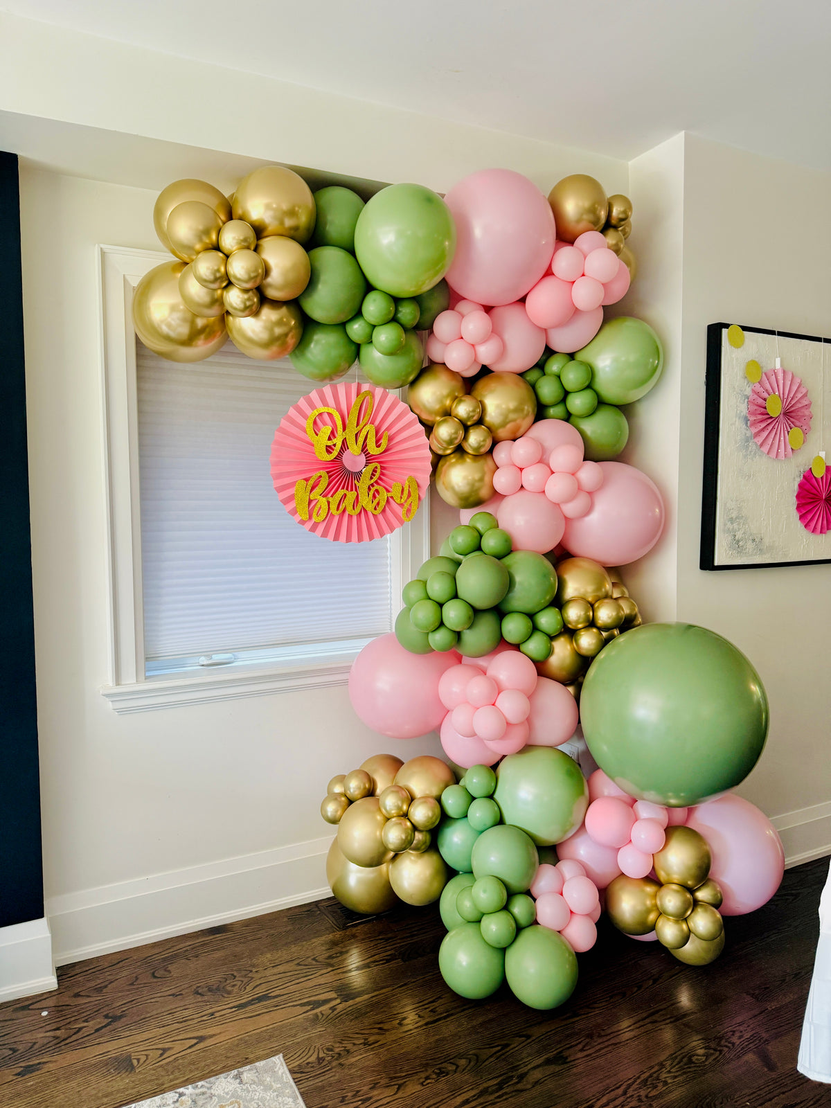 Balloon arch with gold, pink, and green balloons in a room setting.
