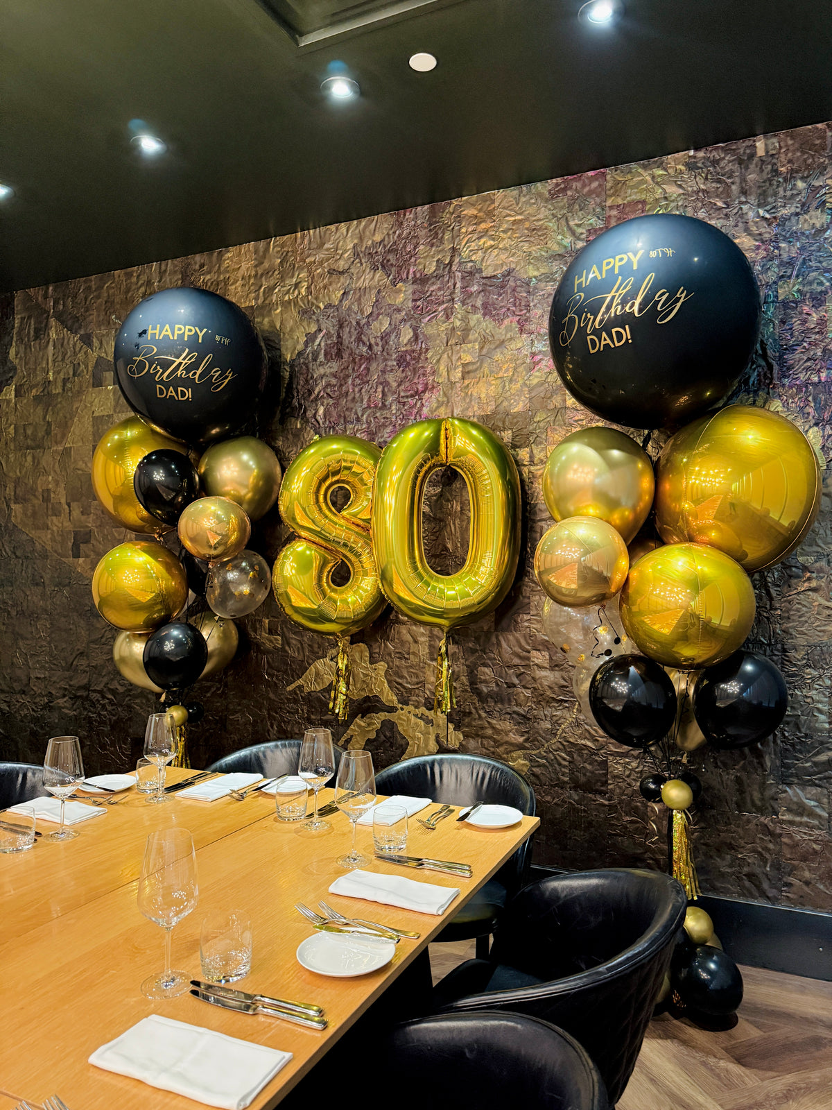 Decorative balloons with 'Happy Birthday Dad' and number '80' in a restaurant setting.