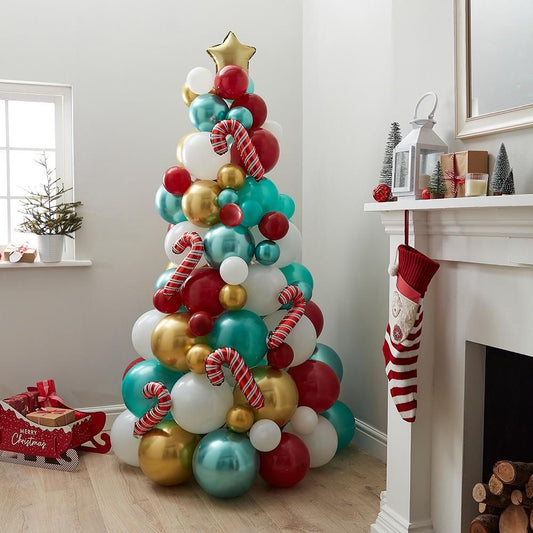 A Christmas-themed balloon tree decoration with red, gold, and white balloons, placed in a room near a fireplace and holiday decorations.