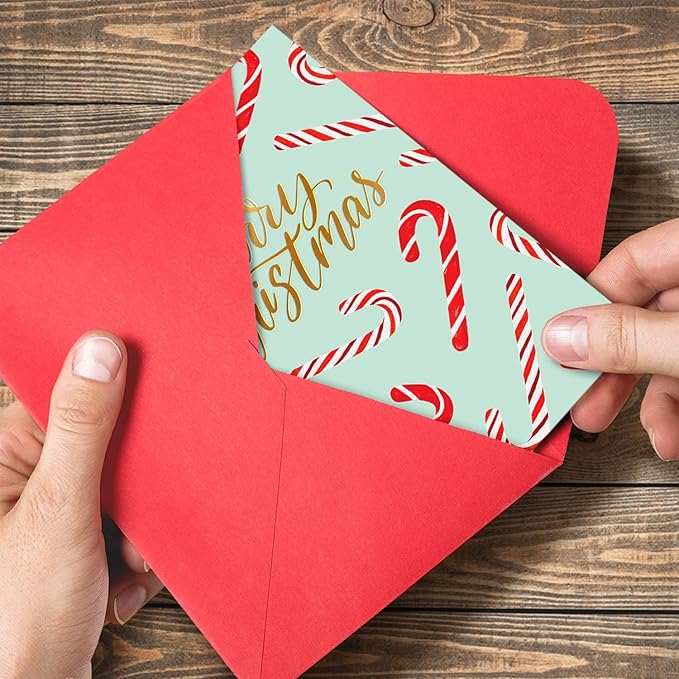Red envelope with a Christmas card featuring candy canes and 'Merry Christmas' text on a wooden surface.