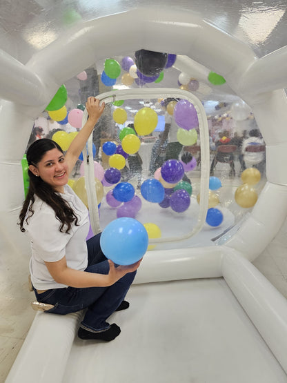 Woman holding a blue balloon inside an inflatable bubble with colorful balloons.