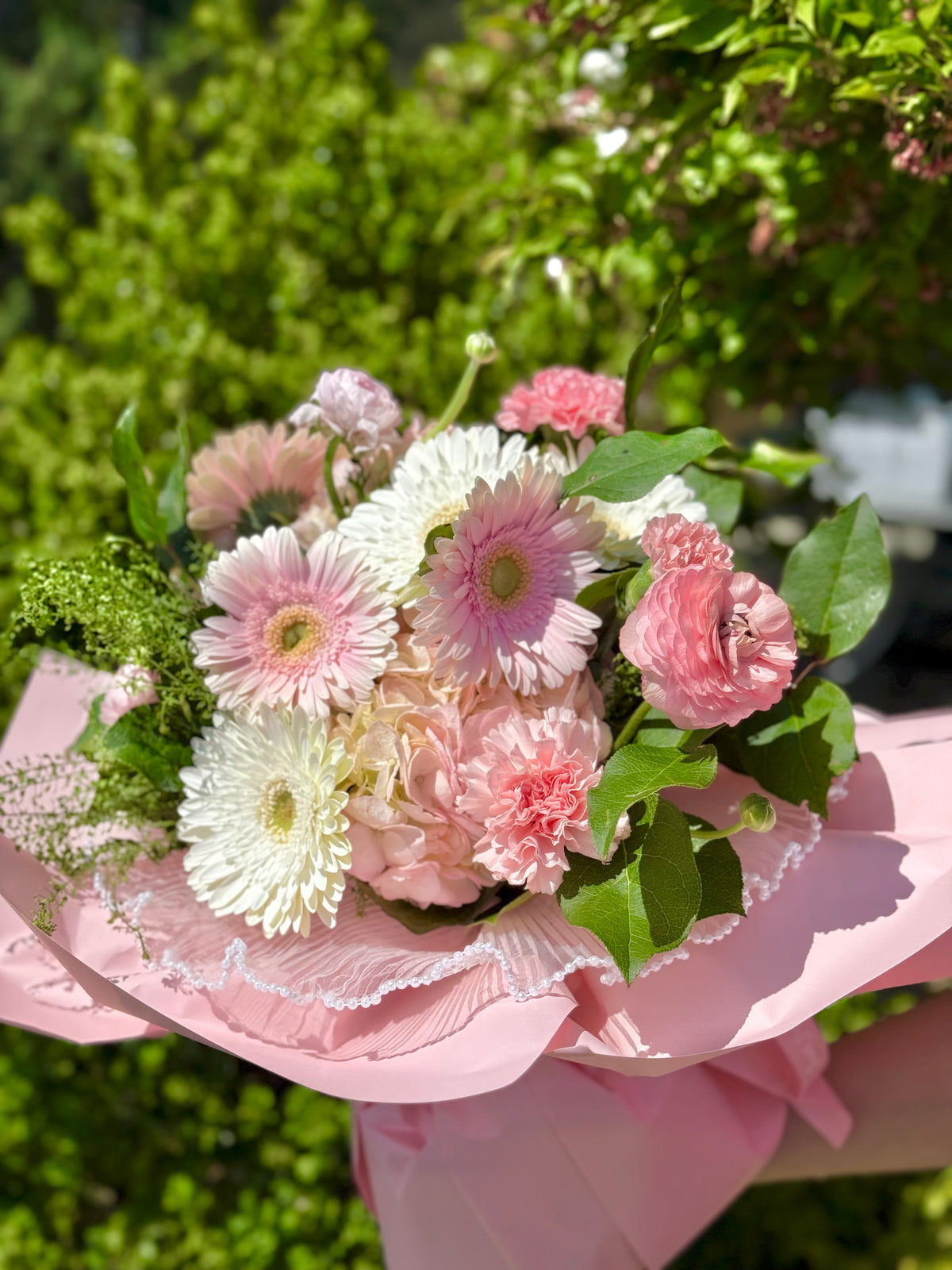 Bouquet of pink and white flowers with green leaves on a pink ribbon.