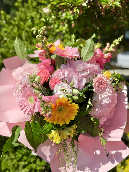 Bouquet of pink and yellow flowers on a pink surface with greenery in the background.