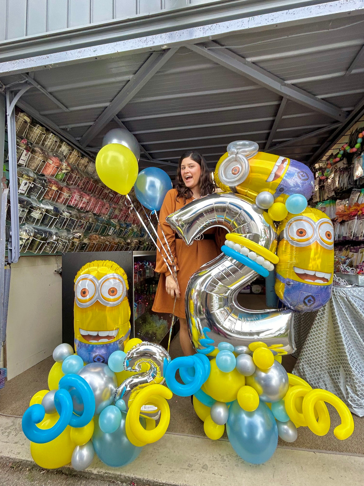 Minion Birthday Balloon Display with Minion character balloons, a large silver number balloon, and festive blue, yellow, and silver balloons.