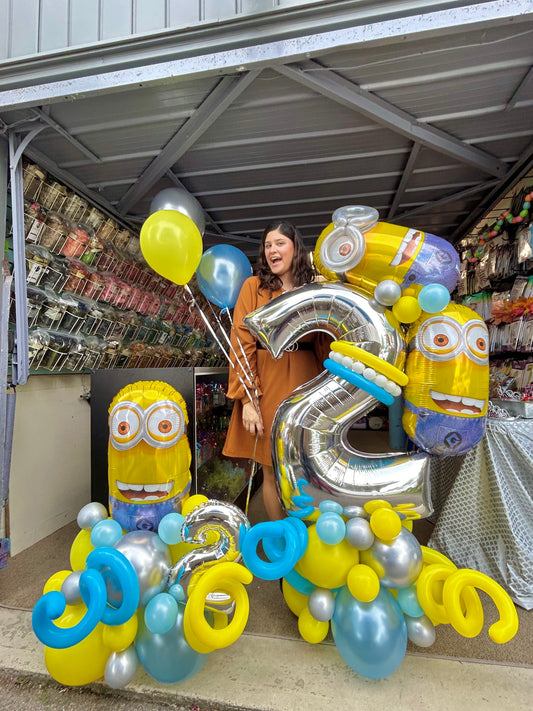 Minion Birthday Balloon Display with Minion character balloons, a large silver number balloon, and festive blue, yellow, and silver balloons.