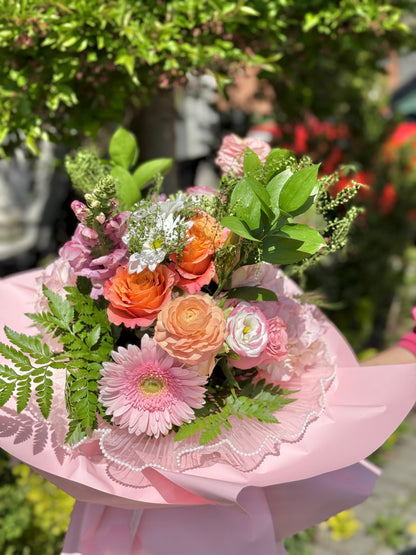 Bouquet of flowers in pink wrapping paper and roses in pink and peach colours. 
