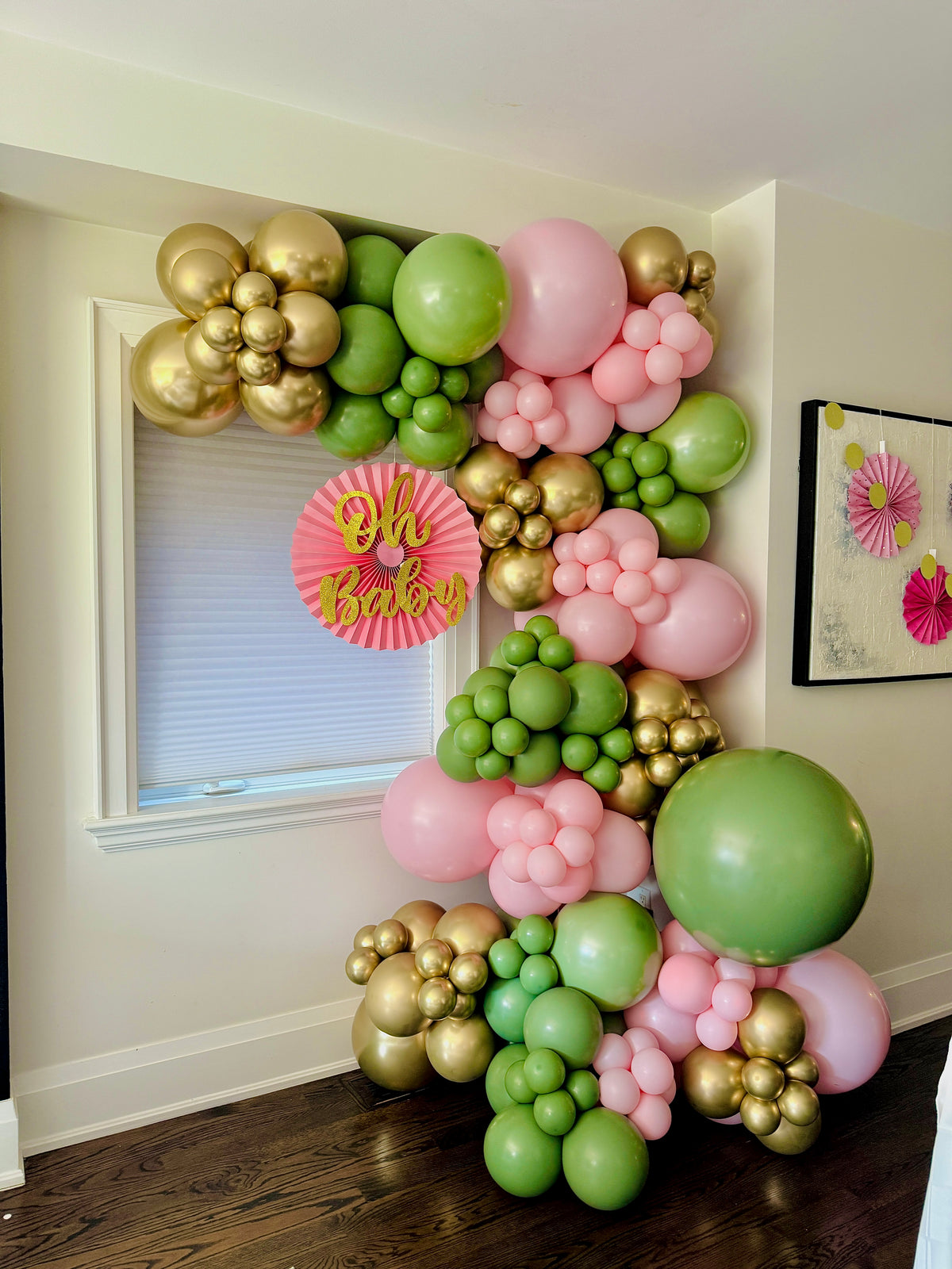 Balloon arch with pink, green, and gold balloons in a room setting.