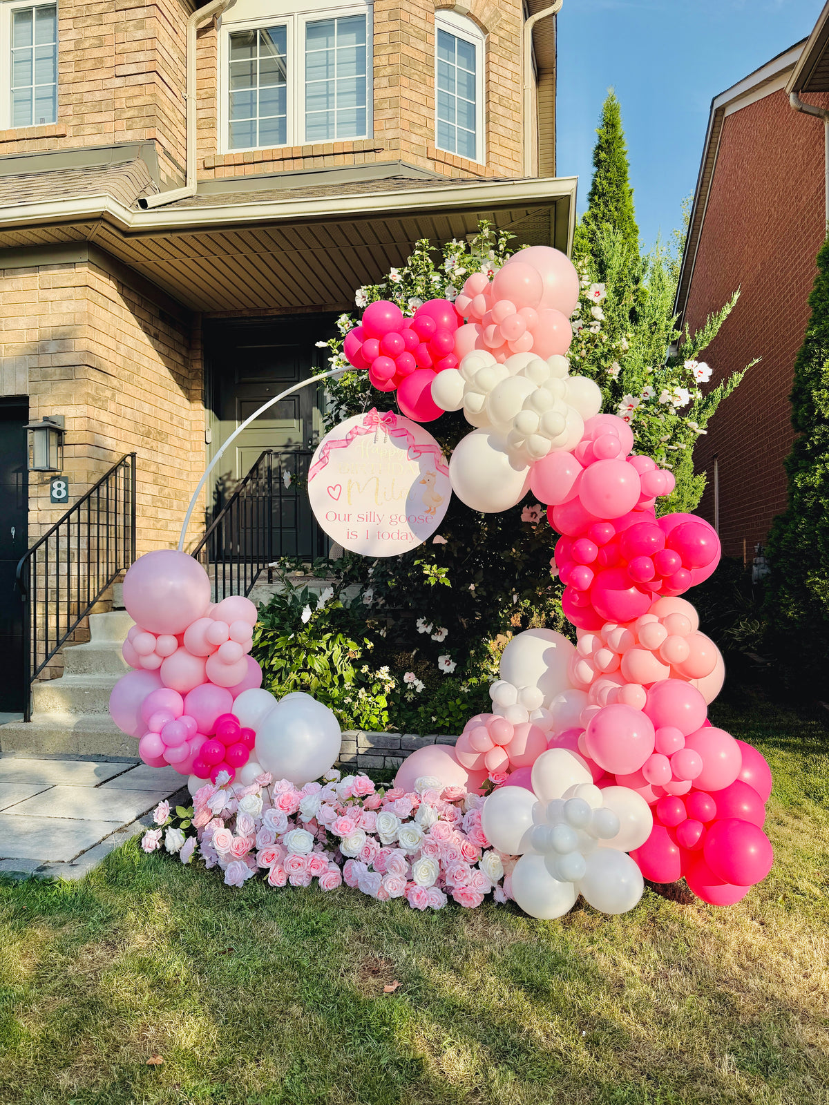 Balloon arch with pink, white, and red balloons in front of a house.