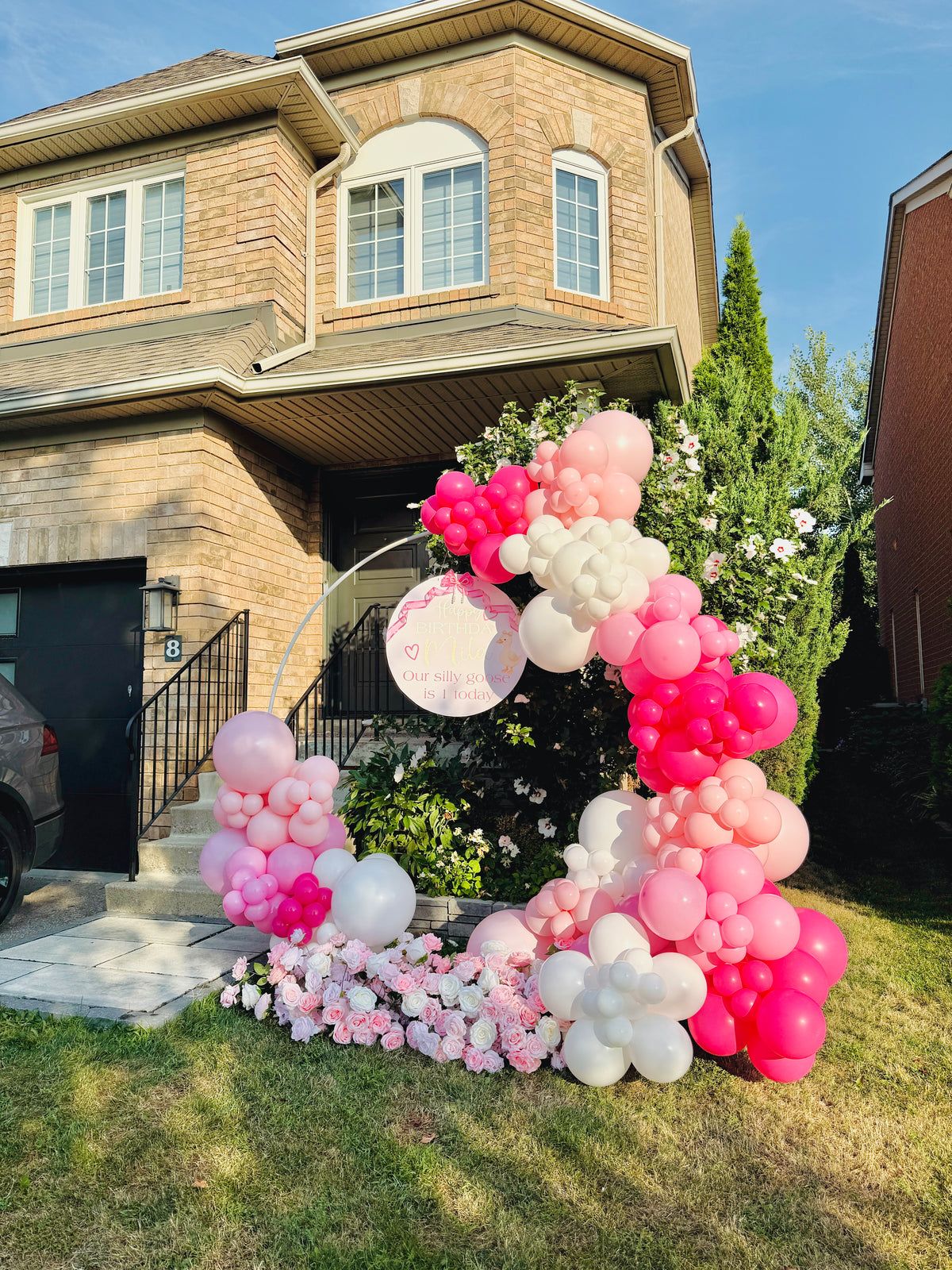 Balloon arch with pink, white, and gray balloons in front of a house.