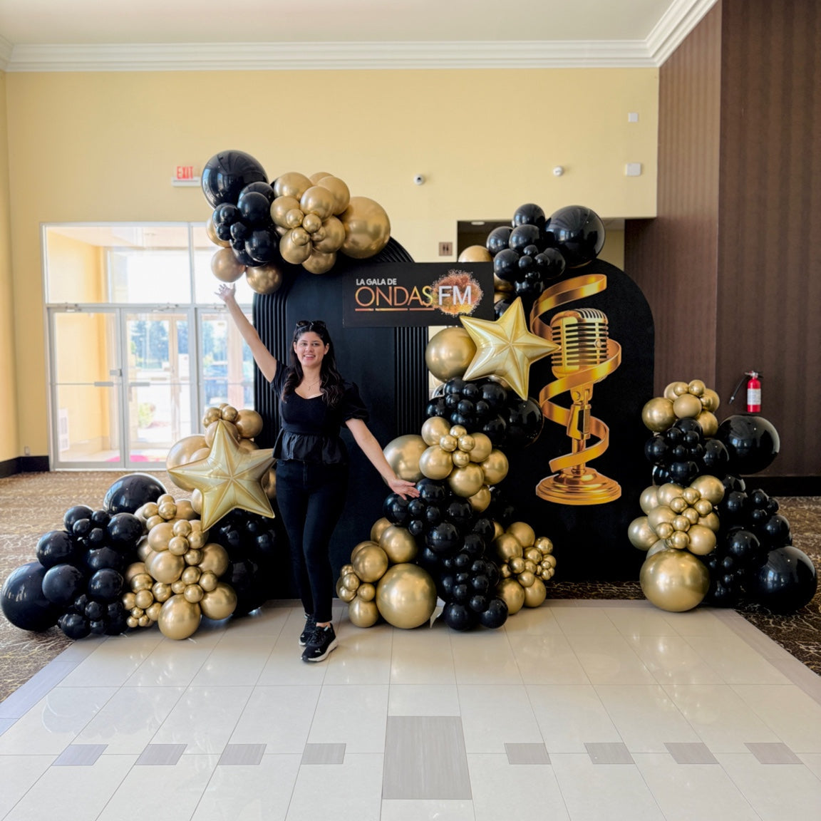 Event decorator standing beside luxury black and gold balloon installation for Ondas FM Gala Toronto.