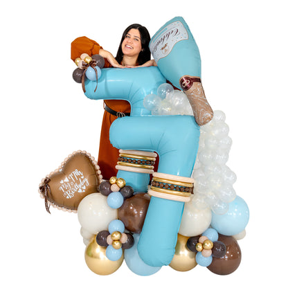 Woman posing behind a turquoise 77 birthday balloon arrangement with a champagne bottle balloon and a birthday heart