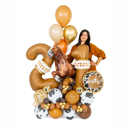 Woman standing beside a western birthday balloon arrangement with bronze number 21, a horse and cow-print balloons, showing its scale at Wooow Balloons Toronto.