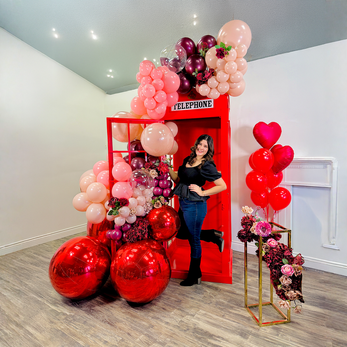 Phone booth balloon backdrop Toronto with romantic red and blush balloons for a Valentine’s Day photo moment